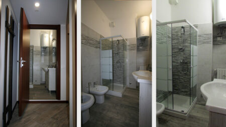 Bagno Camera Matrimoniale Milano con specchio illuminato, asciugamani, lavabo, toilet moderno, doccia con box in vetro, piastrelle grigie decorative, pavimento in legno, illuminazione calda, San Siro Fiera B&B